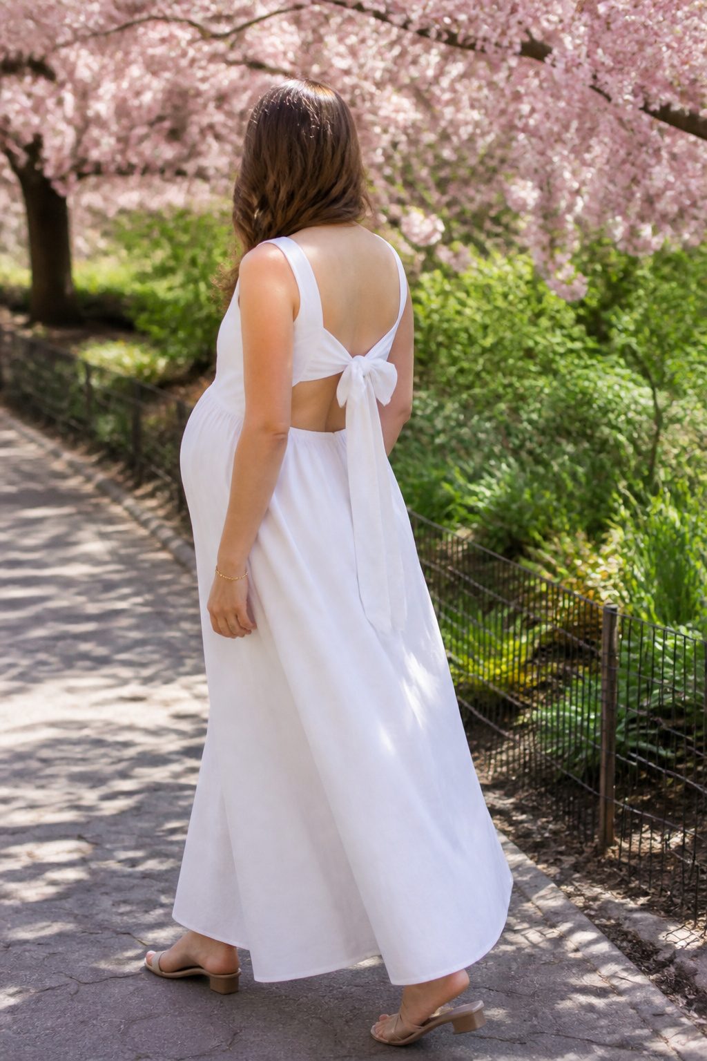 15 Bump Friendly Dresses for 2026: Styles That Grow With You 7 A model wearing a maxi dress with a cutout bow back in a park.