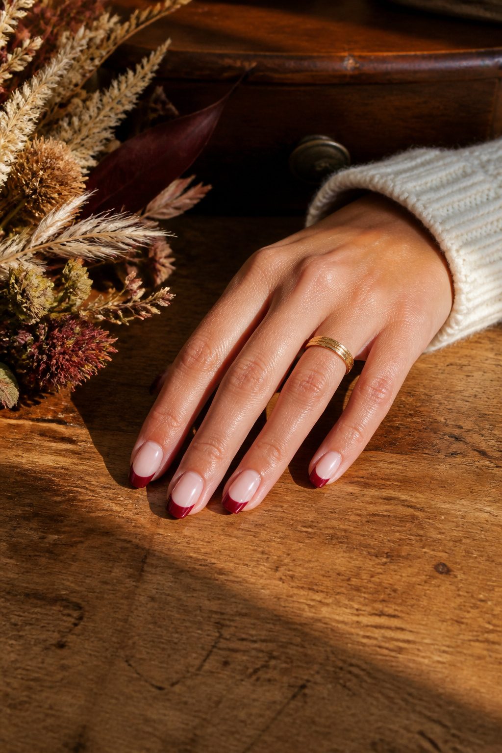 Hand with cherry red French tips resting on a wooden desk.