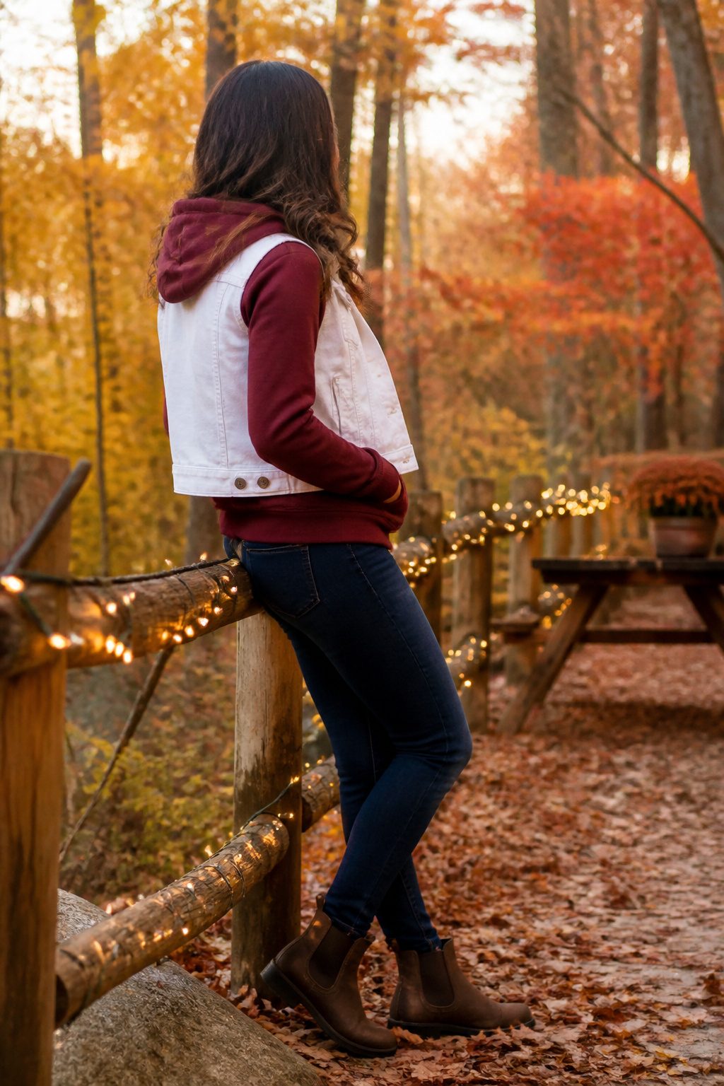 How to Wear a Denim Vest: 13 Outfit Ideas for 2026 13 Model wearing a white denim vest over a burgundy hoodie in autumn leaves.