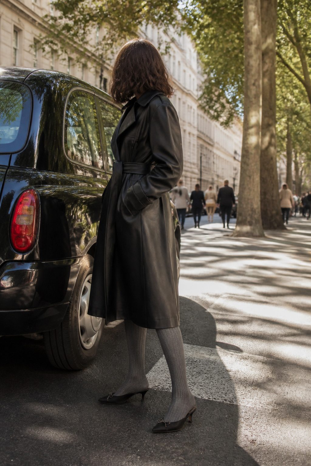A model in a leather trench coat and grey tights stands next to a black cab.
