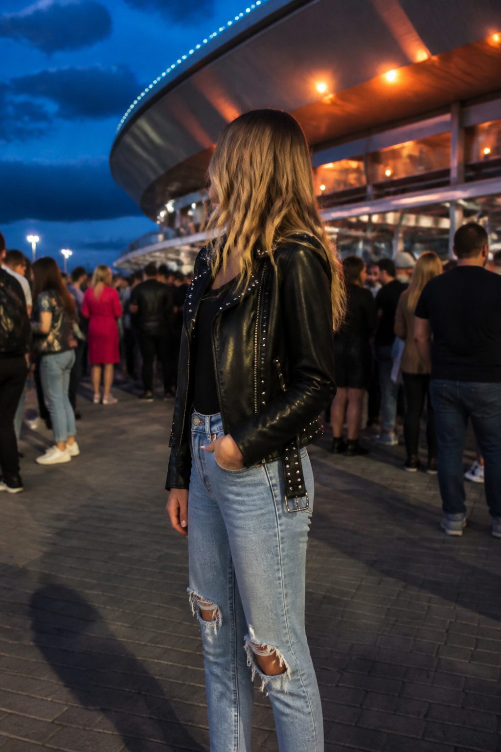 How to Dress for a Pop Concert in 2026 8 A woman wears ripped jeans and a faux leather jacket at a venue.