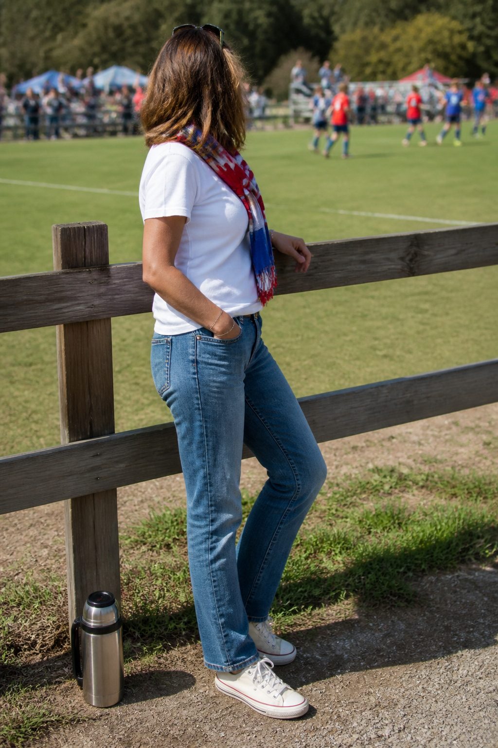 Woman in white tee and straight-leg jeans at a soccer field.